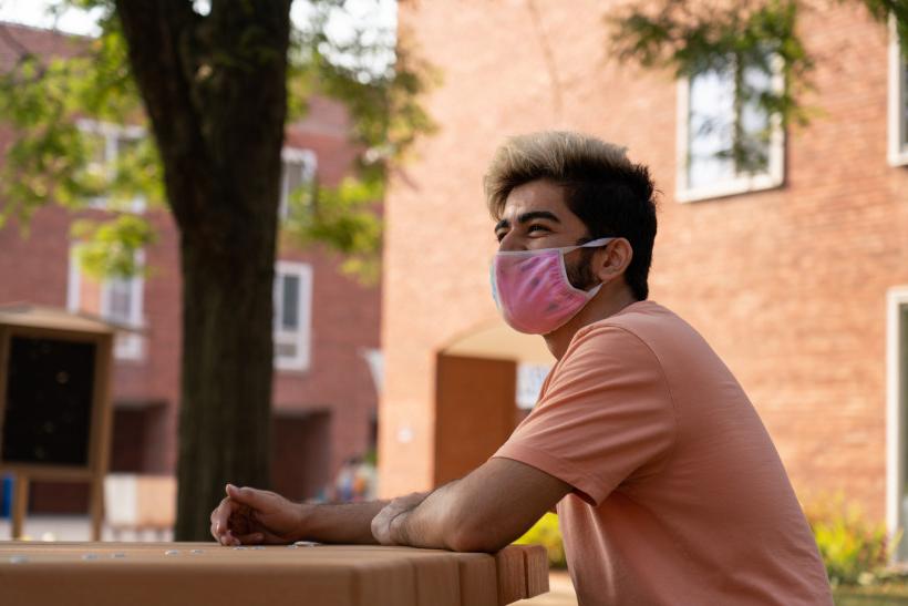 一个学生坐在64年的教学楼外，戴着面具.